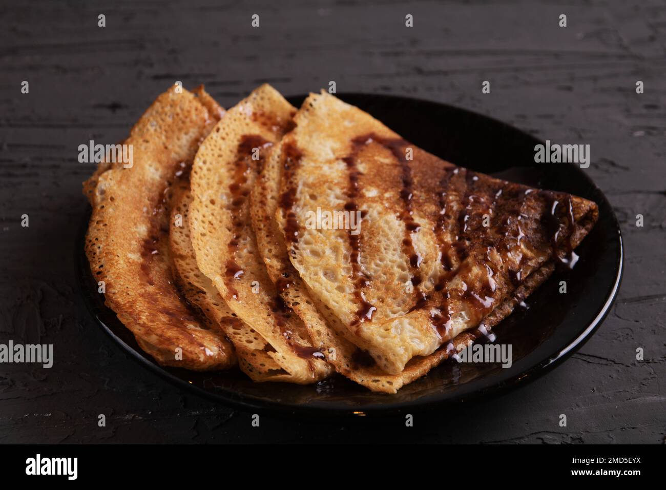 foto tre frittelle a forma di triangolo giacenti su un piatto versato con sciroppo di cioccolato Foto Stock