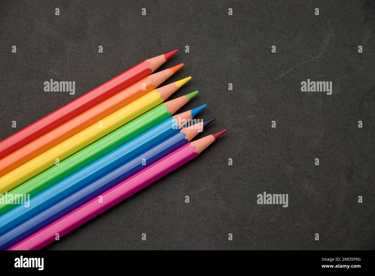 Sfondo per la scuola o il contenuto artistico in cui alcune matite colorate appaiono su una superficie nera testurizzata. Immagine con spazio di copia. Foto Stock