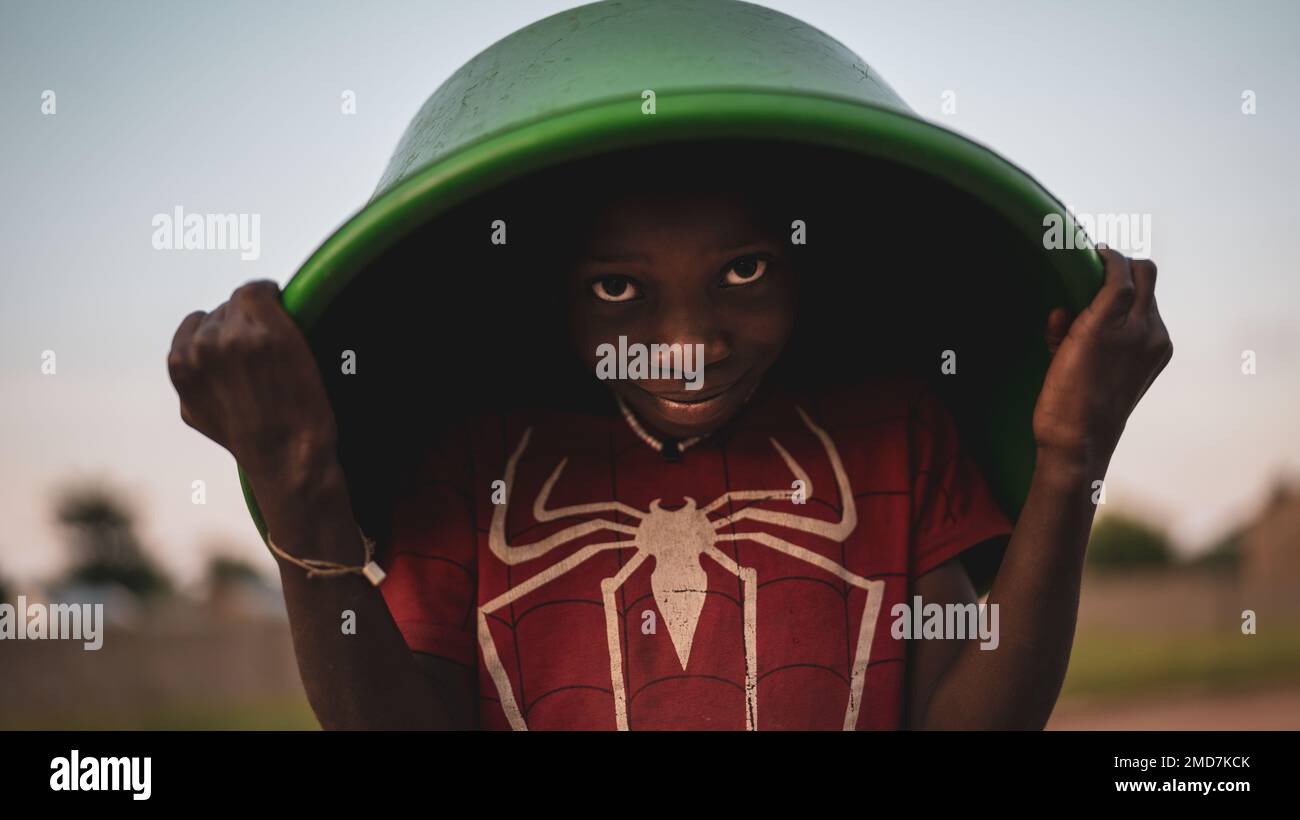 Un bel ragazzo africano in possesso di una ciotola verde per raccogliere l'acqua dal fiume Foto Stock