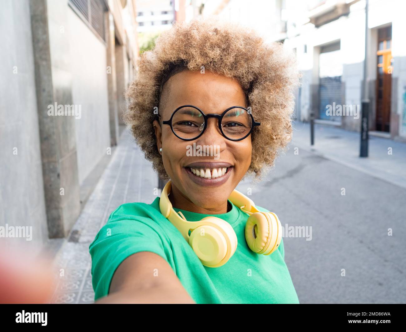 Donna afroamericana sorridente con capelli afro e cuffie che fanno un selfie Foto Stock