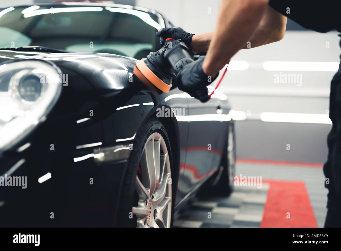 Imriconoscibile maschio esperto lucidando cofano auto o cofano auto con lucidatore orbitale. Scatto in interni. Concetto di dettaglio dell'auto. Foto di alta qualità Foto Stock