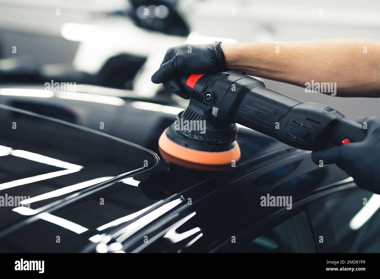 Mani di un uomo con lucidatore orbitale in officina di riparazione lucidando auto sportiva nera. Primo piano. Concetto di dettaglio dell'auto. Foto di alta qualità Foto Stock