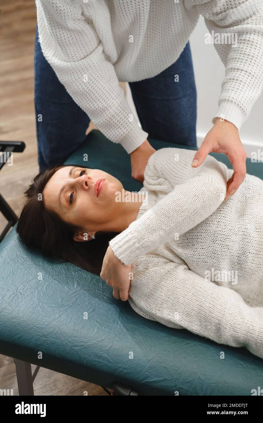 Donna osteopata terapista esame spalla paziente per diagnosi e trattamento. Assistenza professionale e sollievo dal dolore attraverso la terapia manuale Foto Stock