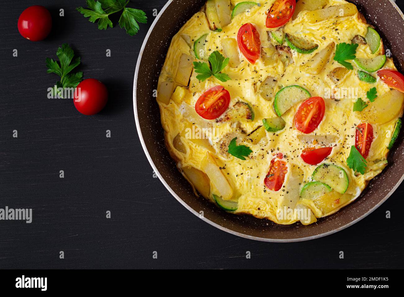 Omelette con pomodori, zucchine e patate su fondo scuro. Dieta sana per la colazione. Gustoso cibo del mattino. Vista dall'alto, disposizione piatta. Foto Stock