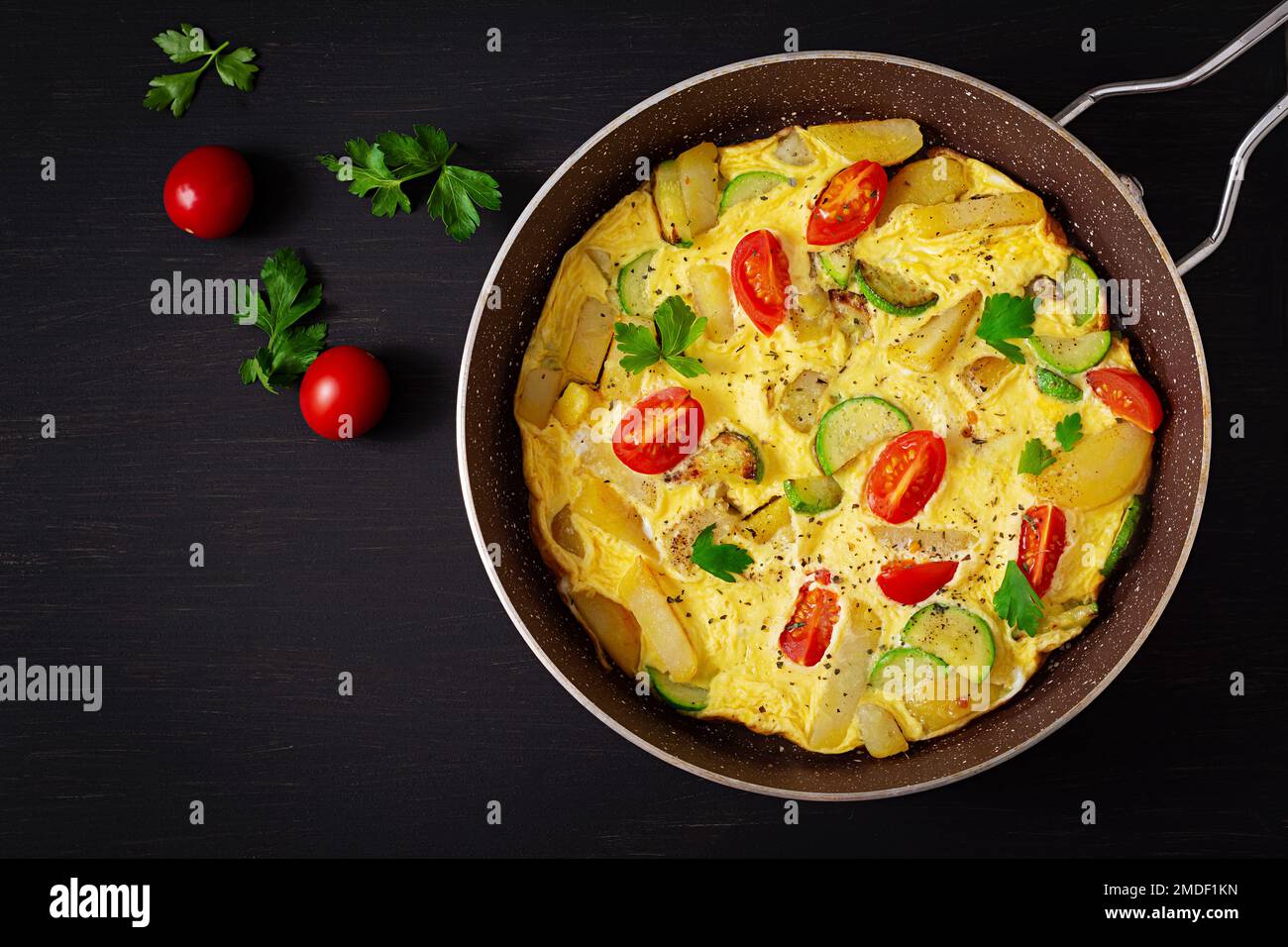 Omelette con pomodori, zucchine e patate su fondo scuro. Dieta sana per la colazione. Gustoso cibo del mattino. Vista dall'alto, disposizione piatta. Foto Stock
