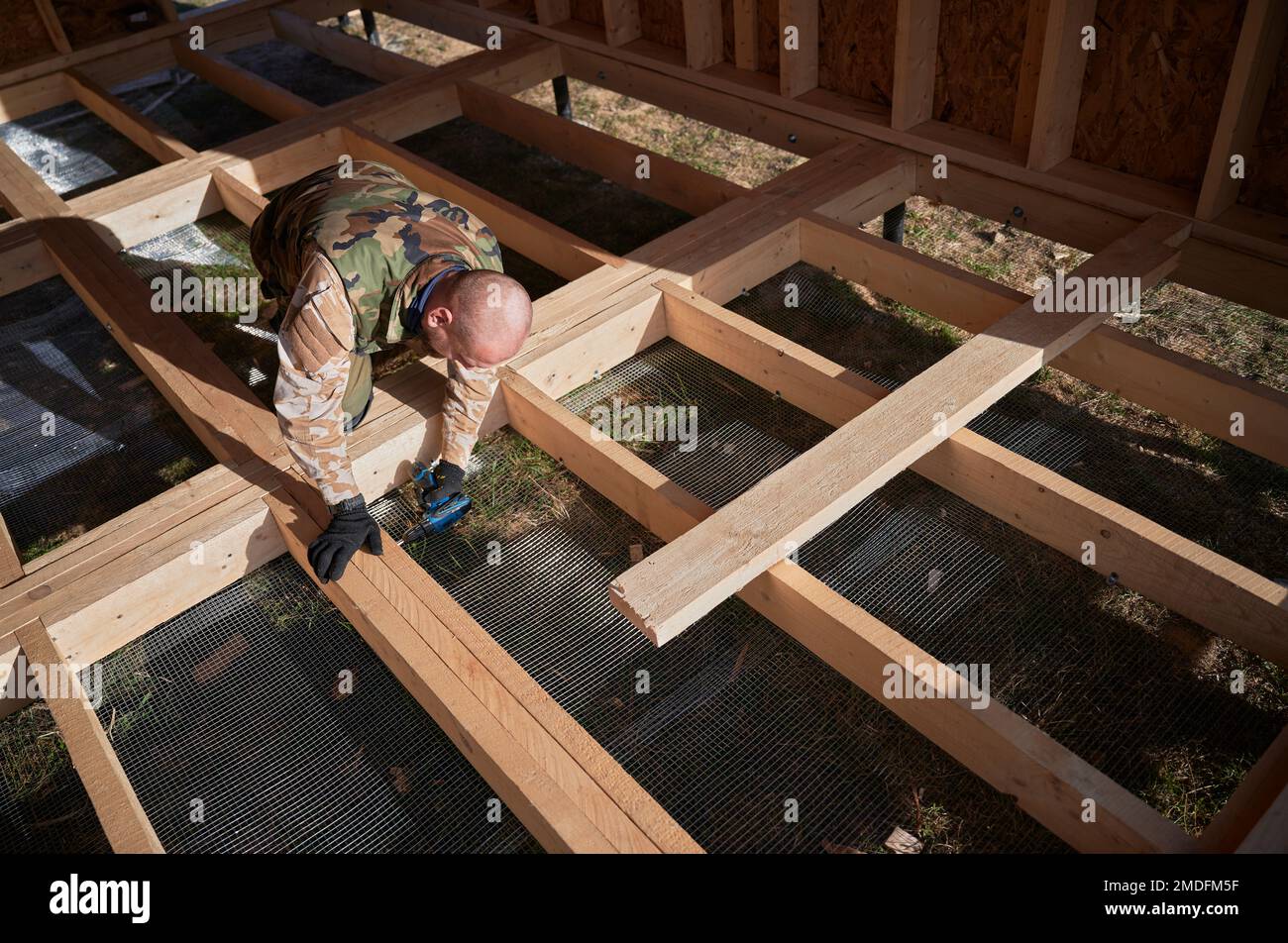 Costruttore maschio che lavora con il cacciavite all'interno del cottage futuro. Uomo lavoratore edificio legno telaio casa. Carpenteria e concetto di costruzione. Foto Stock