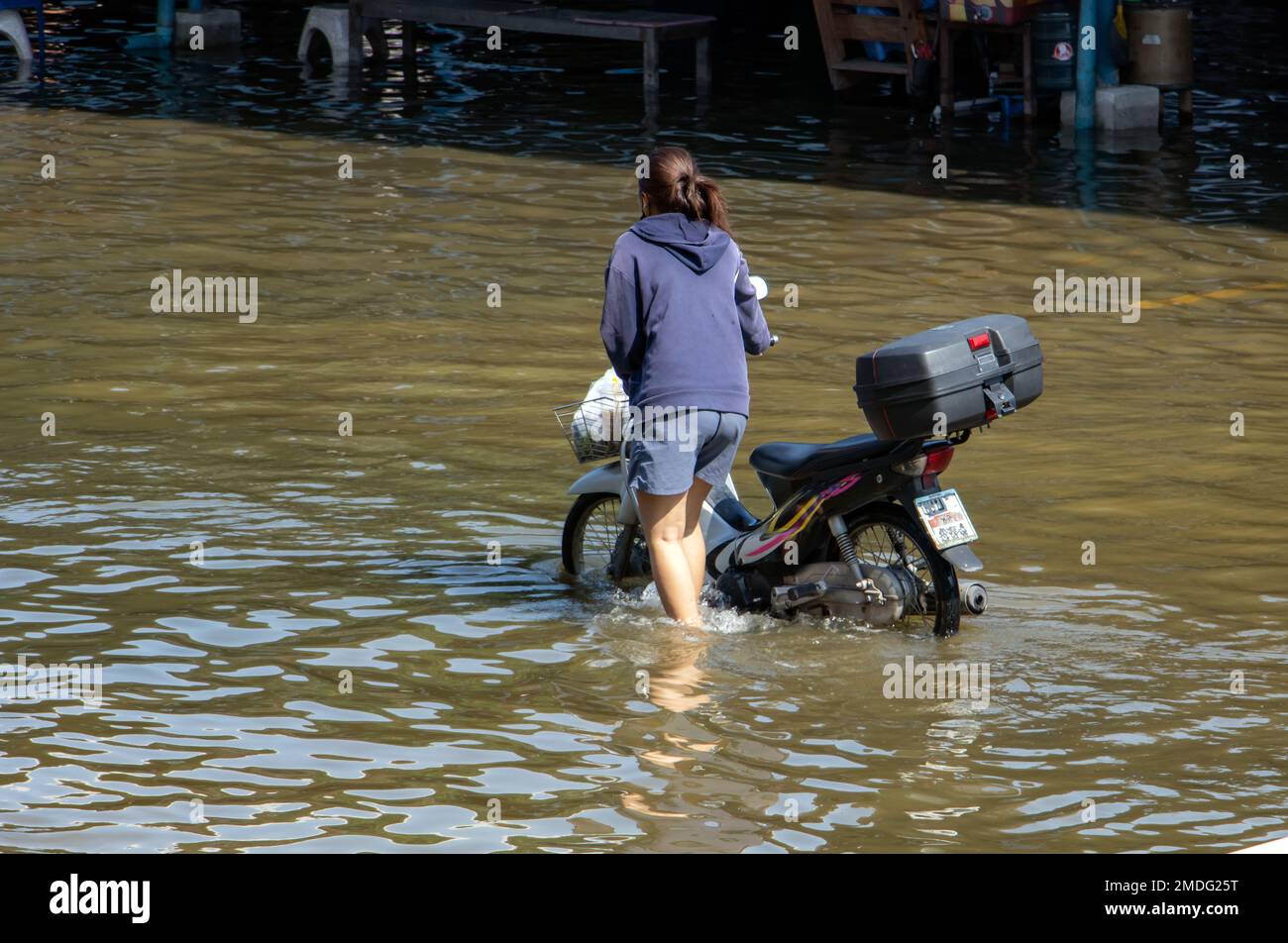 Una donna spinge una moto attraverso una strada allagata, la Thailandia Foto Stock