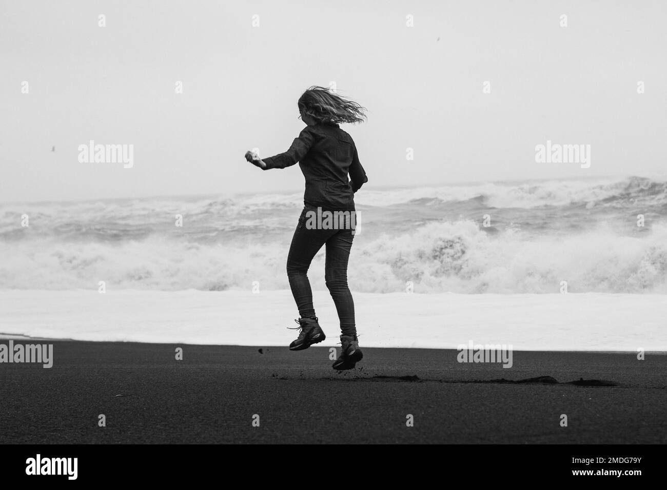 Donna gioiosa che salta sulla spiaggia Reynisfjara fotografia panoramica monocromatica Foto Stock