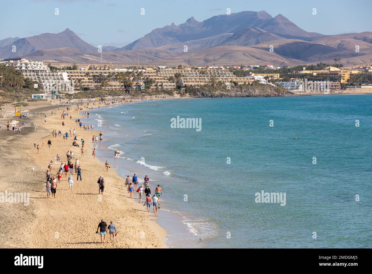 I turisti passeggiando sulla spiaggia a sud di Costa calma. Montagne e strutture turistiche sullo sfondo. Fuerteventura, Isole Canarie. Foto Stock