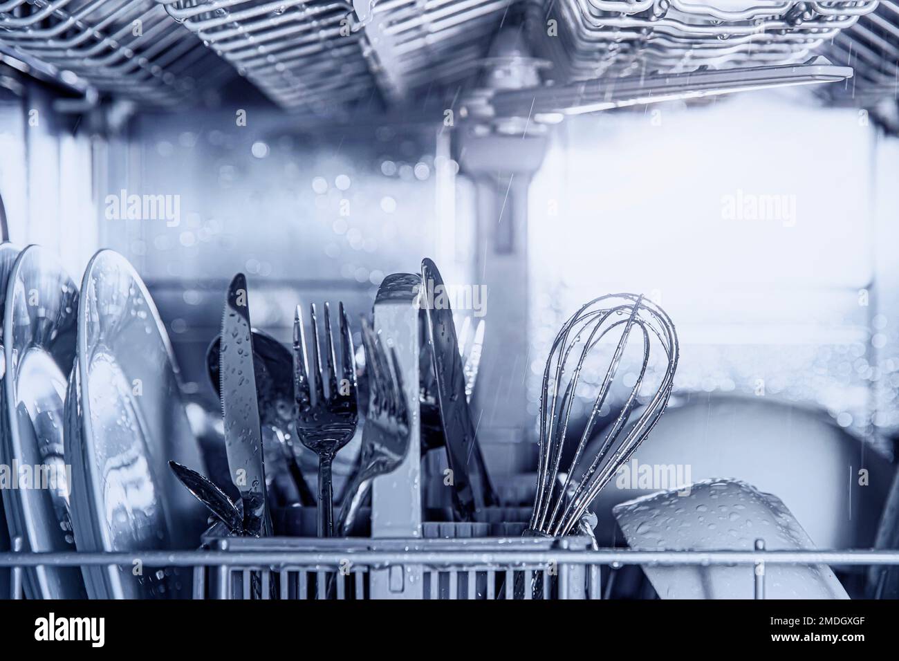 Vista frontale della macchina lavastoviglie automatica aperta in acciaio inox da incasso completamente integrata con controllo dall'alto, dotata di utensili puliti, posate, bicchieri, piatti, piatti all'interno di una moderna cucina casalinga Foto Stock