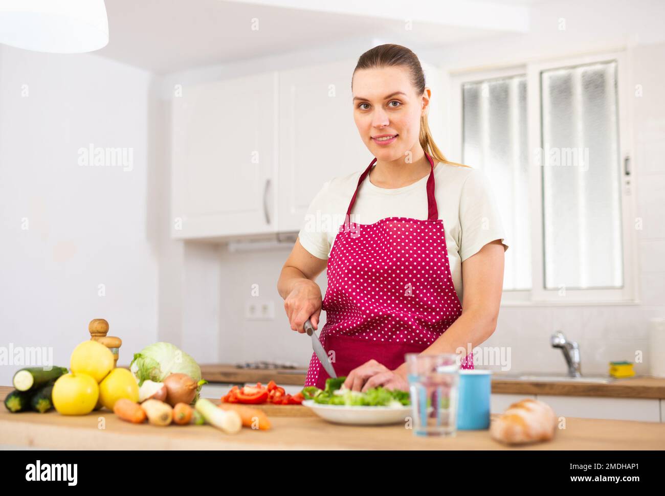 La donna positiva sta tagliando le verdure per l'insalata in cucina nel paese Foto Stock