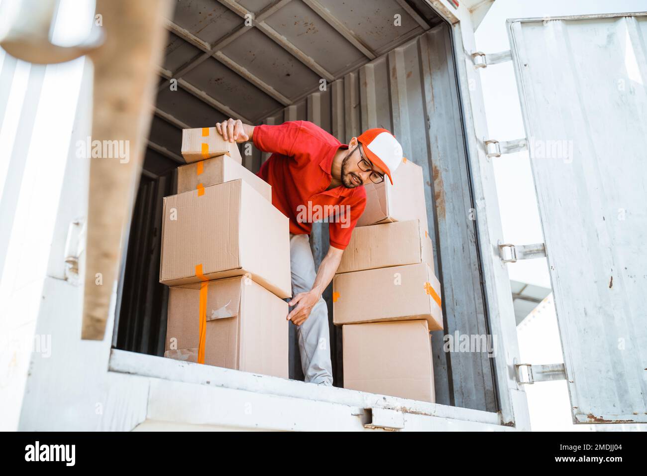 l'addetto alla consegna in rosso scarica diverse scatole da un contenitore Foto Stock