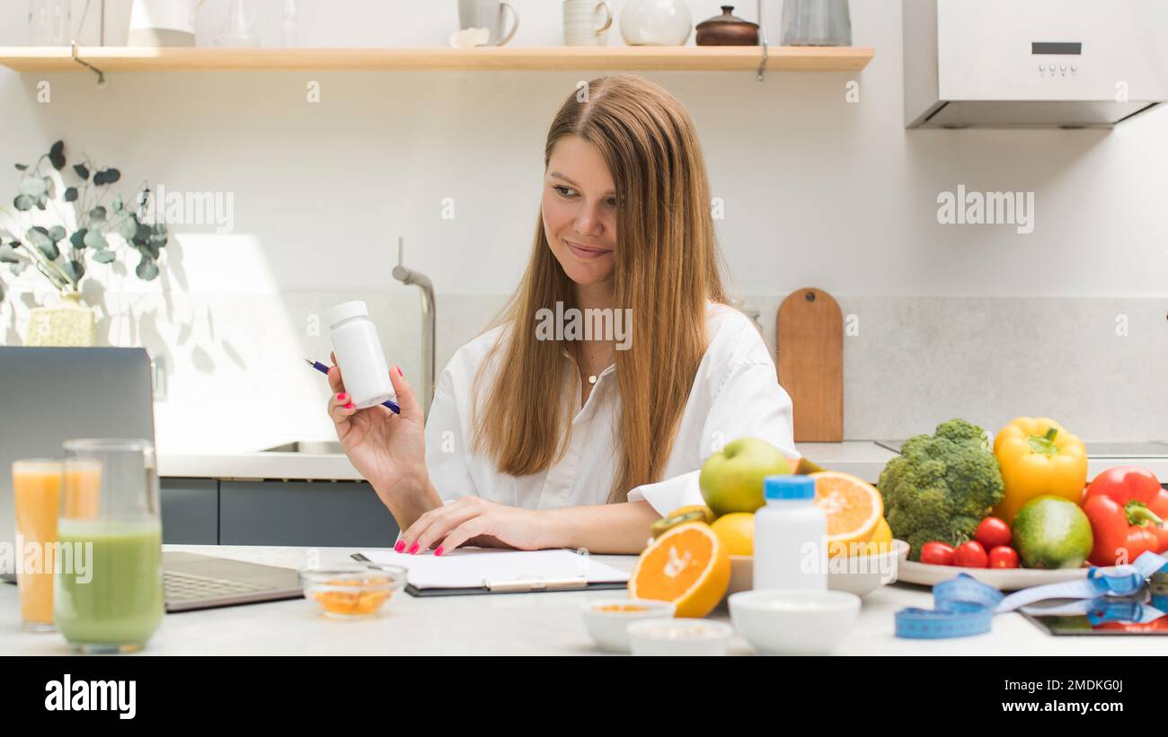 Un giovane nutrizionista consiglia un paziente online su prendere farmaci, integratori alimentari, mostrando un vasetto di vitamine. Foto Stock