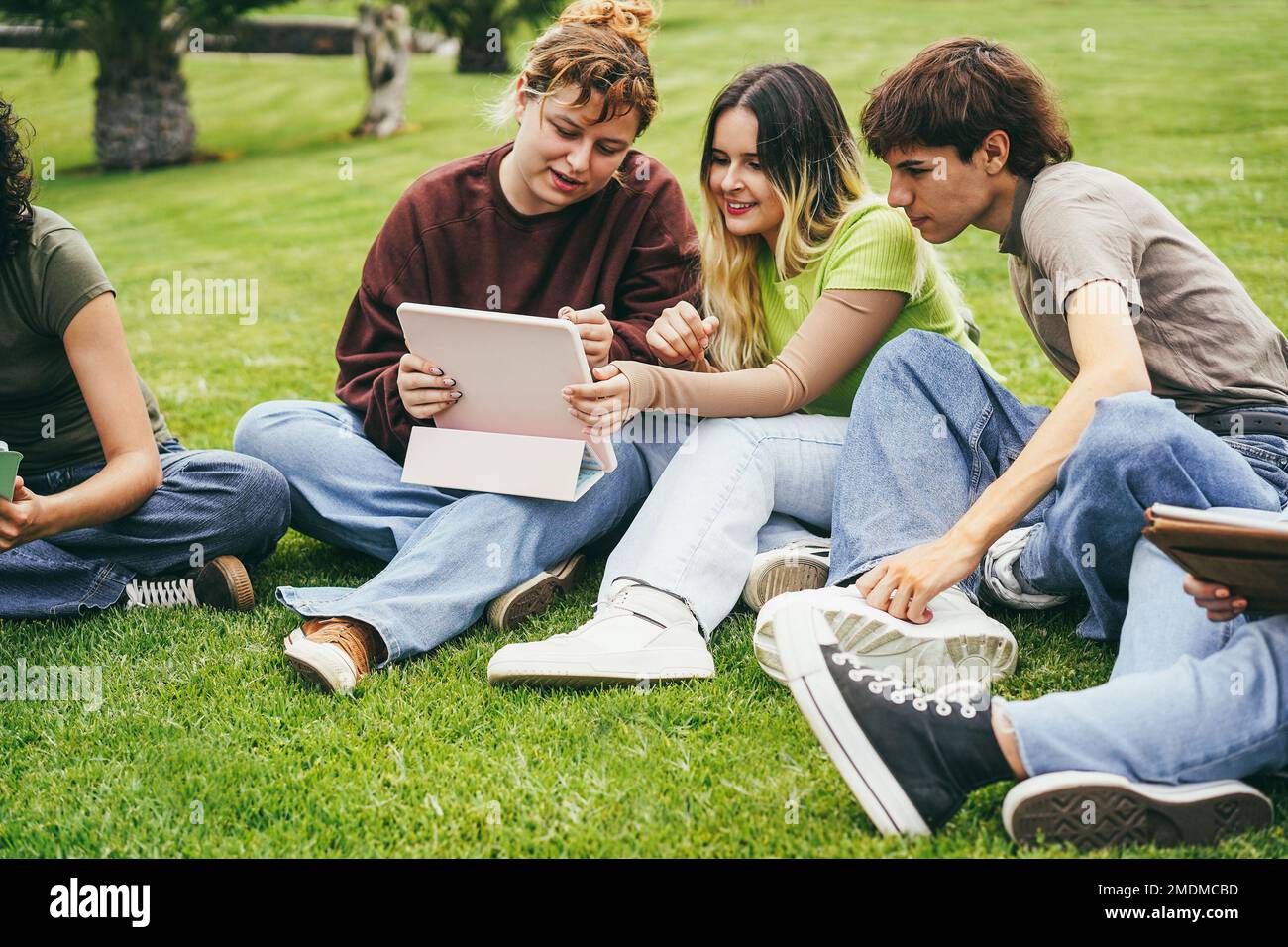 Giovani amici che studiano insieme all'aperto seduti nel campus universitario del parco - concentratevi sul tablet con le mani in mano Foto Stock