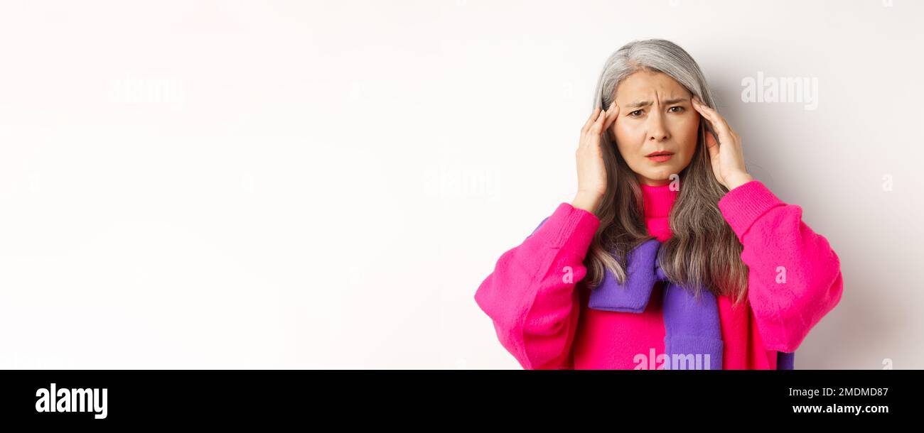 Primo piano di moda donna anziana sensazione di malessere, toccando la testa e grimacing da mal di testa, lamentarsi di emicrania, sfondo bianco Foto Stock
