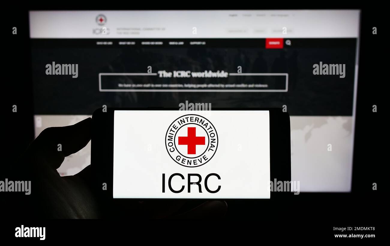 Persona che tiene il cellulare con il logo del Comitato Internazionale della Croce Rossa (CICR) sullo schermo di fronte alla pagina web. Messa a fuoco sul display del telefono. Foto Stock
