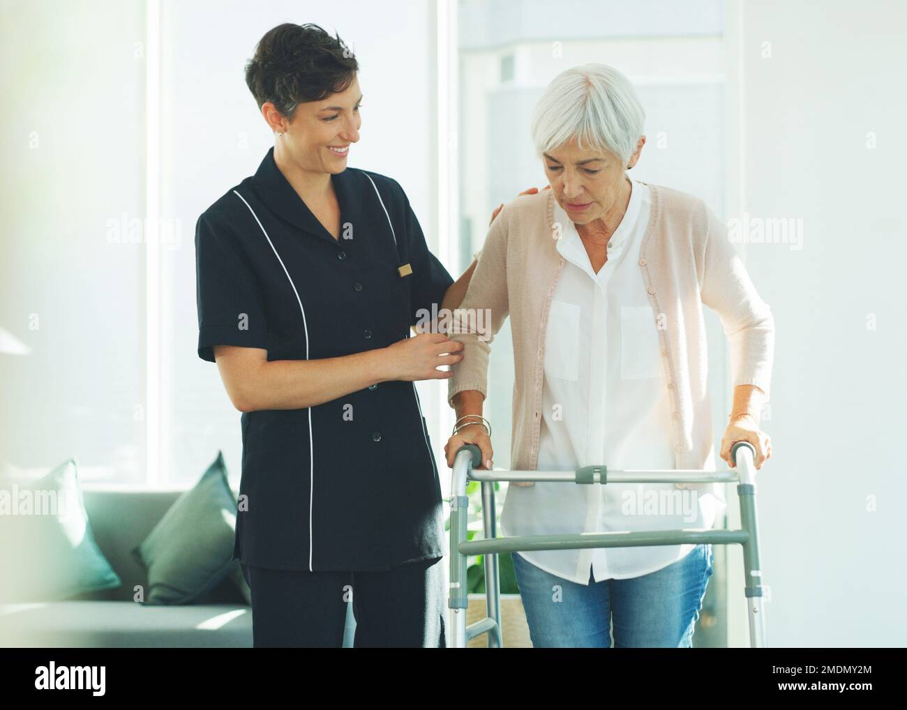 Ti prego, aiutami. un giovane operatore sanitario attraente che aiuta il paziente anziano a camminare con un camminatore in una casa di cura. Foto Stock