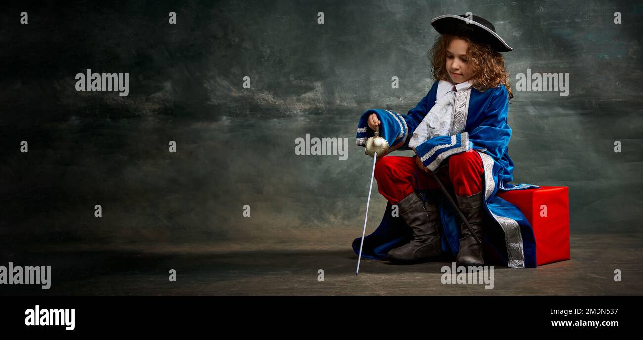 Banner con seria bambina premurosa che indossa il costume di principe, musketeer che posa su sfondo scuro stile vintage. Moda, teatro, bellezza Foto Stock