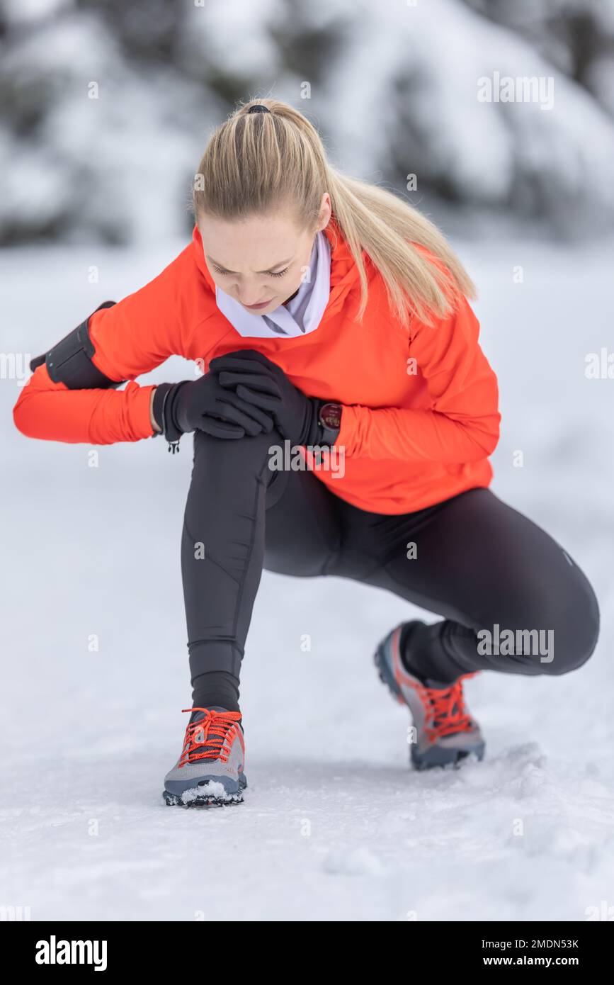 Una giovane donna in forma tiene un ginocchio rinforzato dopo aver tendere il suo legamento crociato durante l'allenamento di fondo sulla neve durante la stagione invernale. Foto Stock
