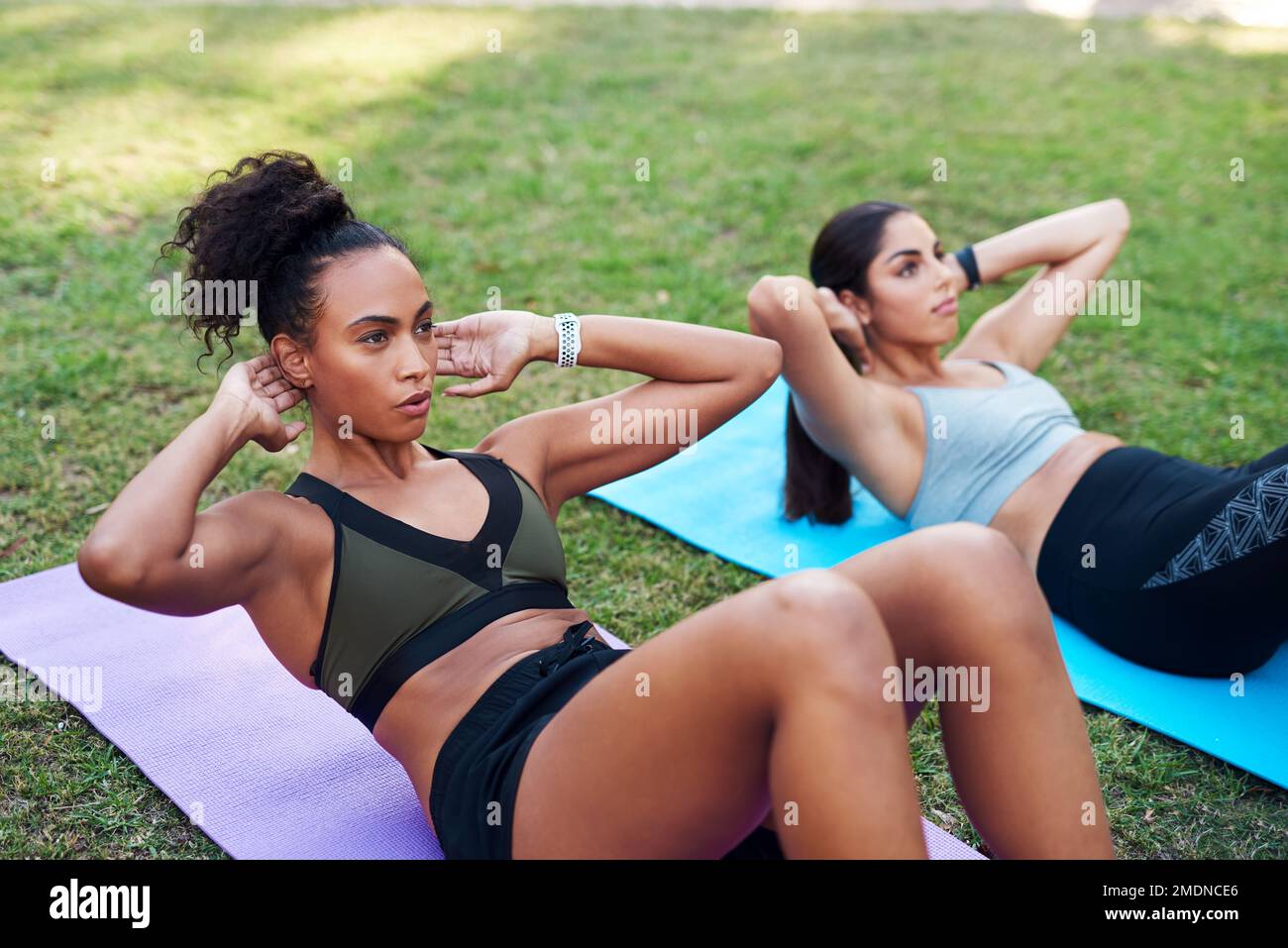 Nessun dolore, nessun guadagno. due giovani donne attraenti che eseguono esercizi di base l'una accanto all'altra nel parco durante il giorno. Foto Stock