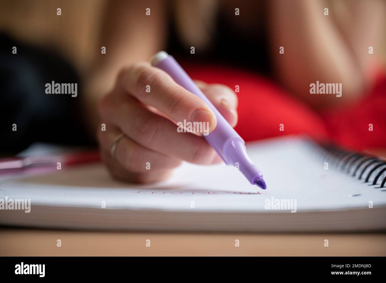 Vista di primo piano ad angolo basso di una studentessa che studia, sottolineando note importanti in un notebook con un pennarello viola. Foto Stock