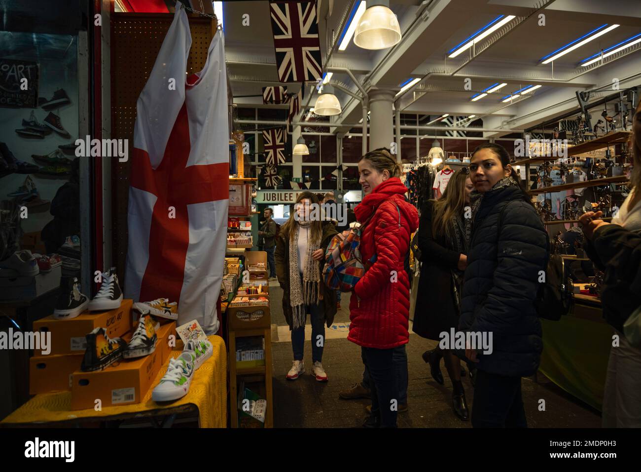 Londra - 02 27 2022: Mercato a Covent Garden con le donne che passeggiando attraverso bancarelle di knick-knacks e con la bandiera dell'Inghilterra Foto Stock