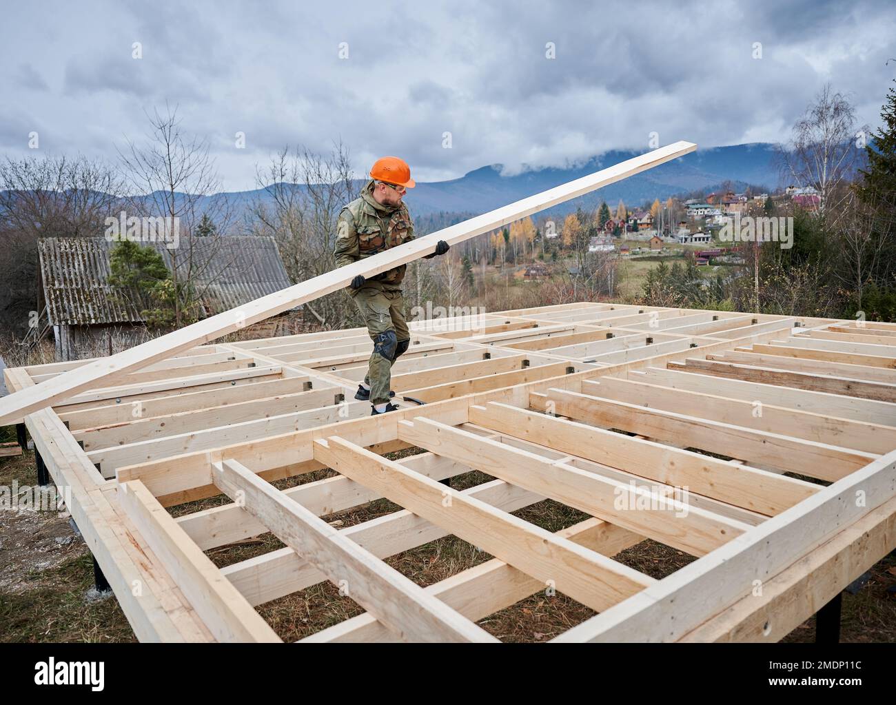 Uomo lavoratore costruire casa telaio in legno su fondazione palo. Falegname che trasporta asse di legno. Concetto di Falegnameria. Foto Stock
