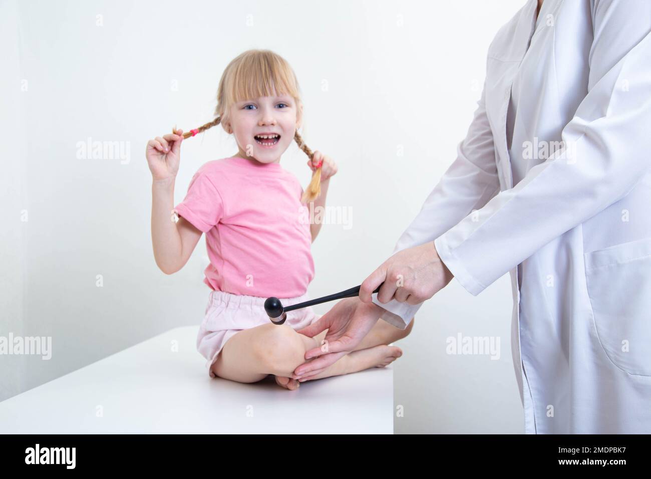 Una ragazza gioiosa di 5 anni con pigtail alla ricezione di un neurologo  pediatrico. Un neurologo controlla il riflesso del ginocchio con un martello  neurologico, m Foto stock - Alamy