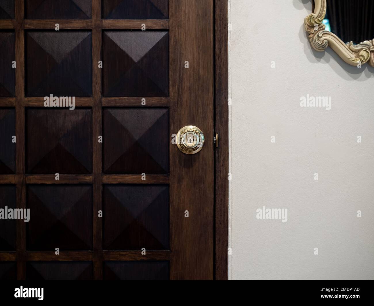Pomolo della porta in ottone vecchio lusso su una porta in legno vintage con specchio vintage appeso a pareti bianche nella camera bianca. Foto Stock