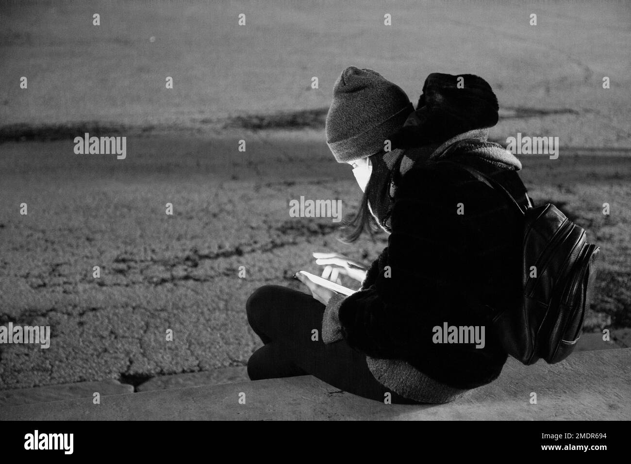 Donna di notte seduta su una panchina controlla il suo smartphone Foto Stock