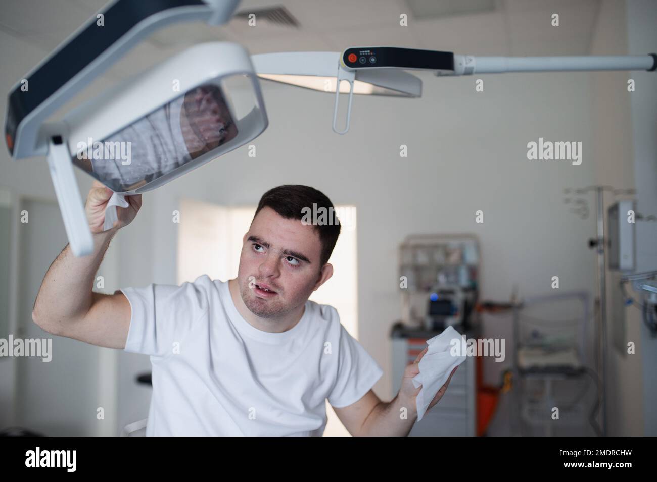 Giovane uomo con giù syndome che lavora in ospedale come aiutante, più pulito. Concetto di integrazione di persone con disabilità nella società. Foto Stock