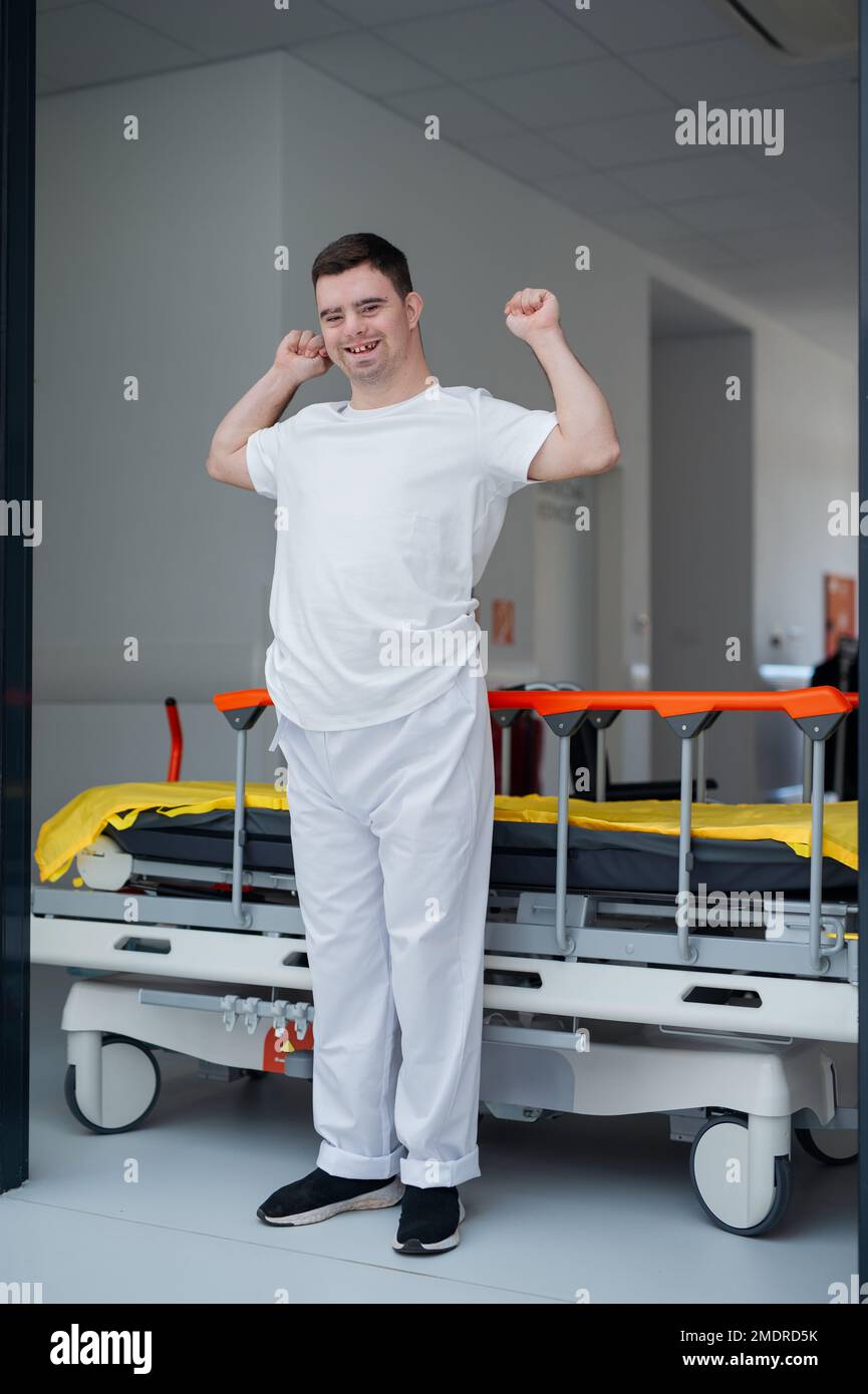 Giovane uomo con giù syndome che lavora in ospedale come caregiver. Concetto di integrazione di persone con disabilità nella società. Foto Stock