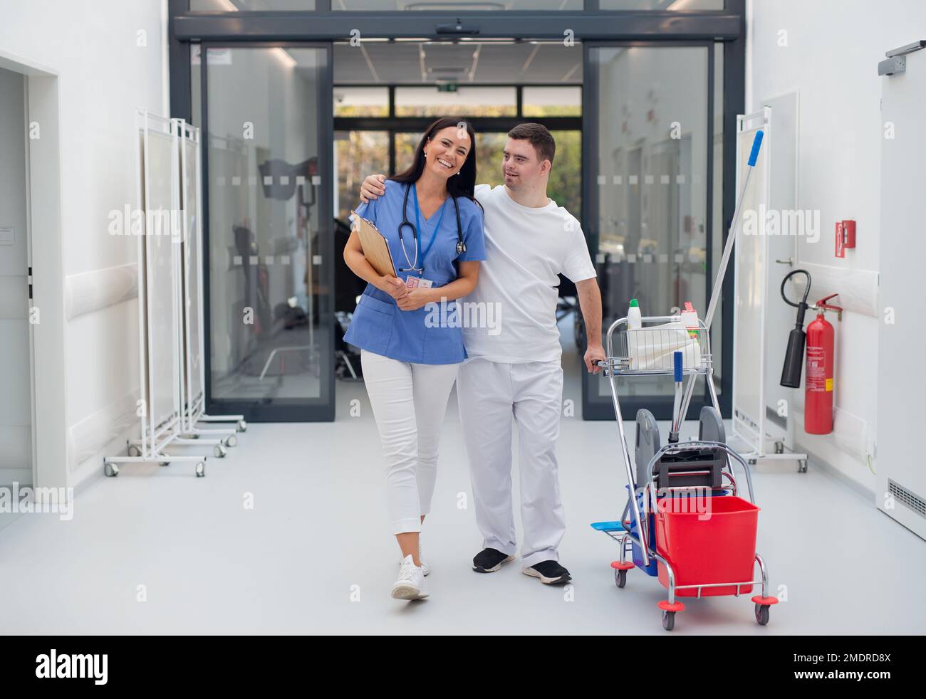 Giovane uomo con sindrome di Down che lavora in un ospedale come più pulito, parlando con l'infermiera, divertendosi. Concpet di integrazione persone con disabilità in Foto Stock