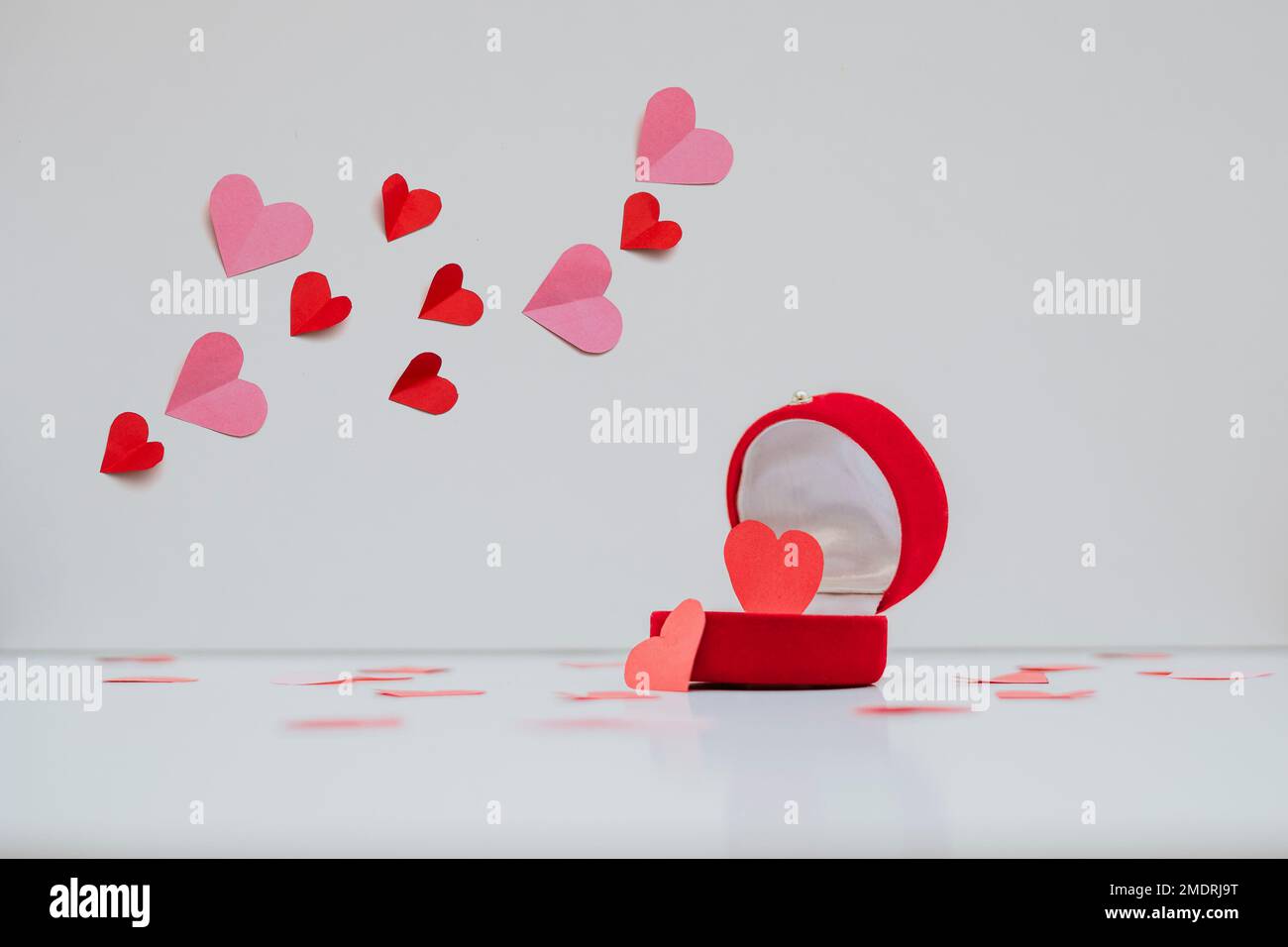 I cuori di carta in due colori volano sopra la scatola dell'anello in cui un cuore è disposto. Gli elementi decorativi sono isolati su uno sfondo bianco Foto Stock