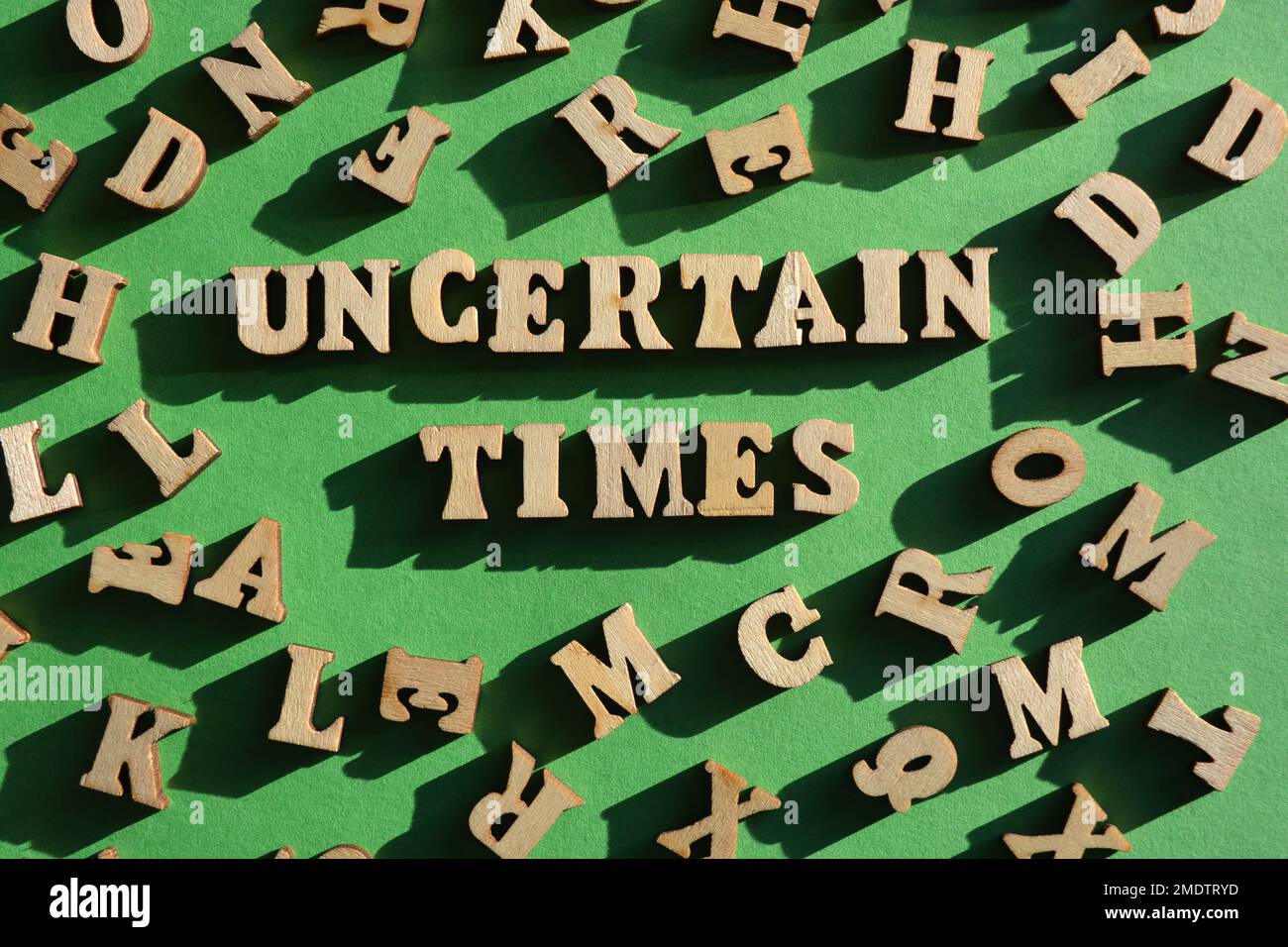 Tempi incerti, le parole in lettere alfabetiche di legno circondano da lettere casuali su sfondo verde Foto Stock