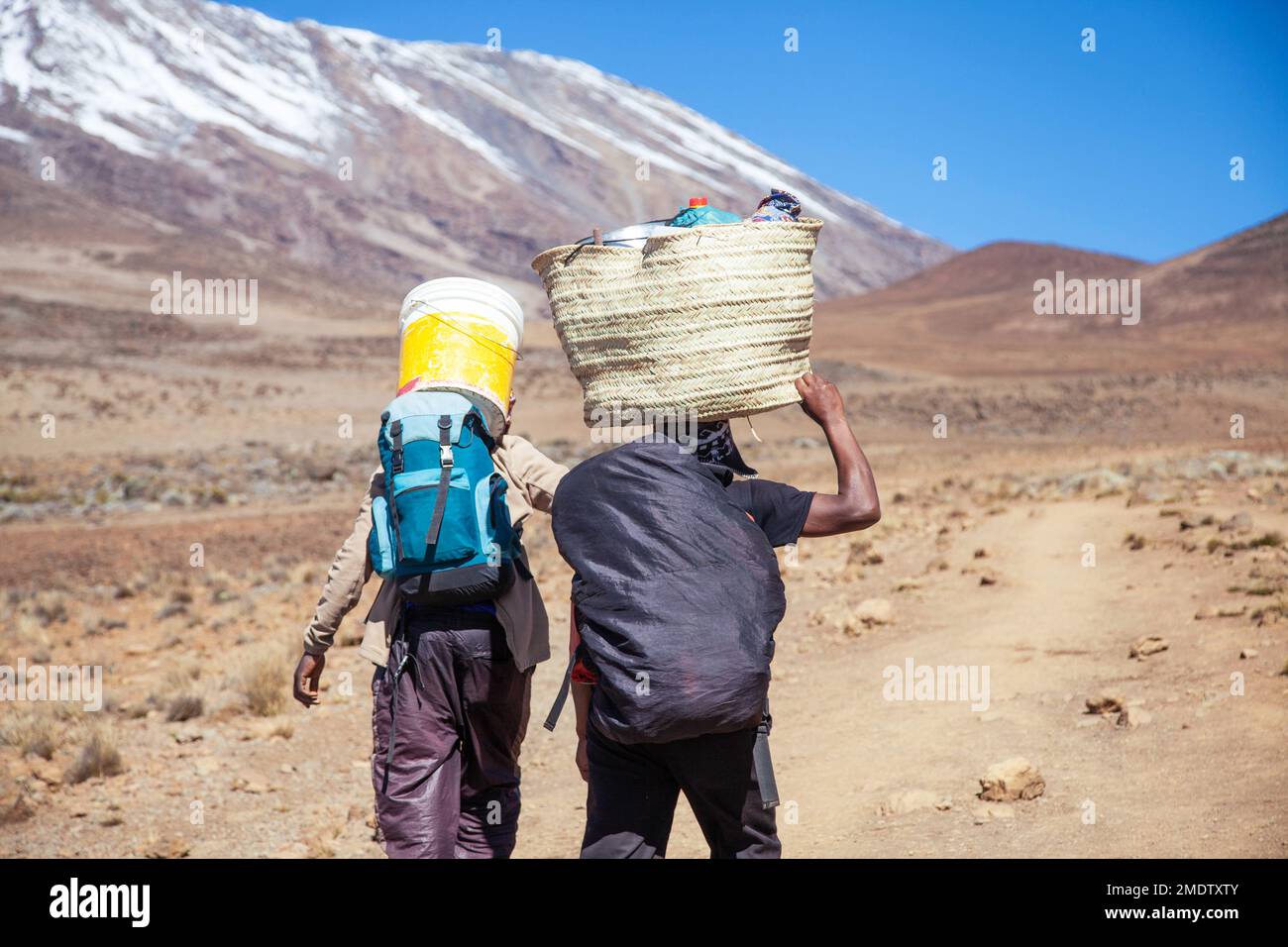 I portieri che trasportano il carico pesante sulla sua parte posteriore camminano lungo la strada. Foto Stock