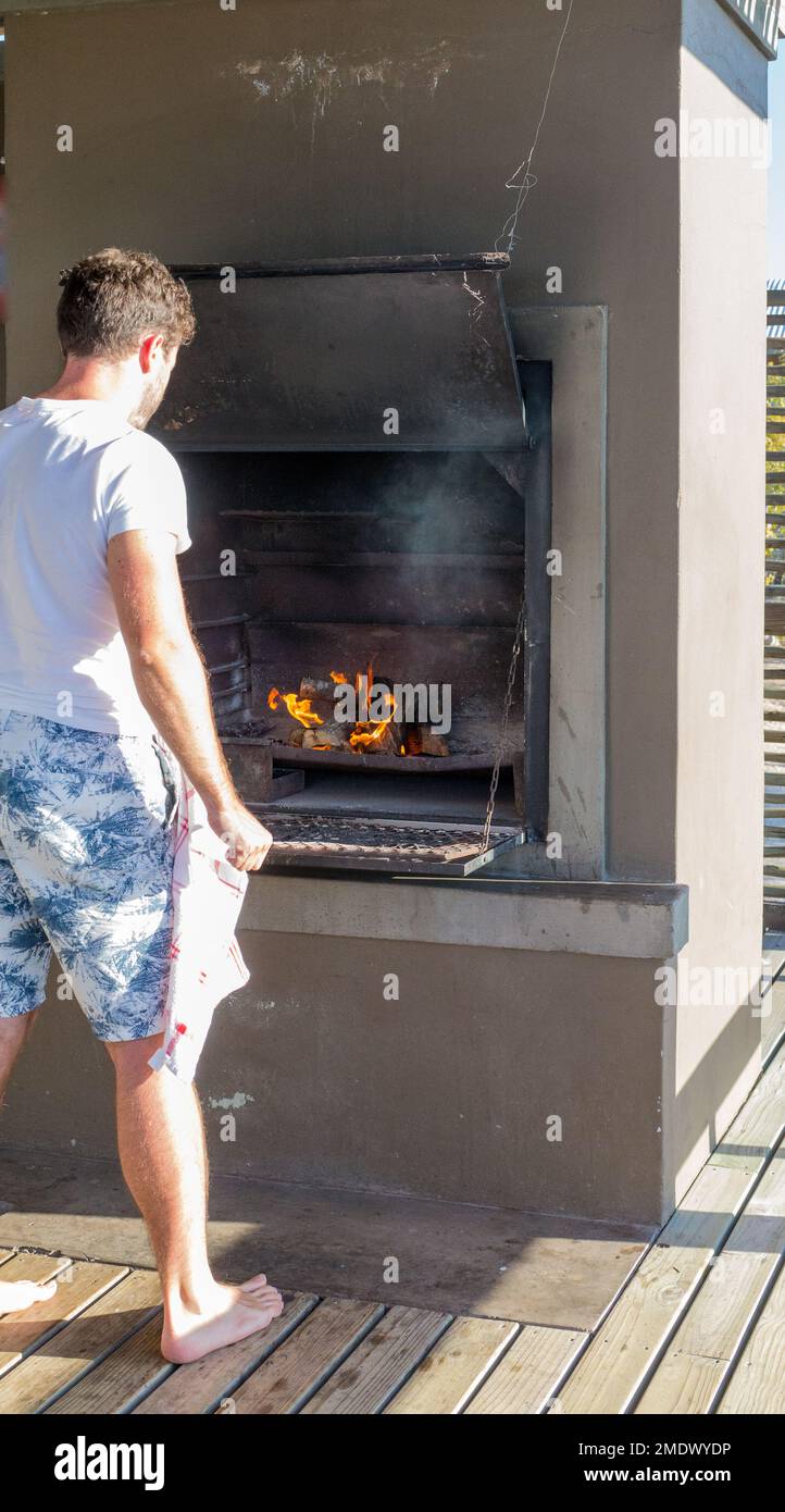 Giornata del patrimonio sudafricano braai, braaivleis o fuoco barbecue con un giovane uomo nei suoi 20 anni che si accingono al fuoco illuminato e che guardano le fiamme Foto Stock