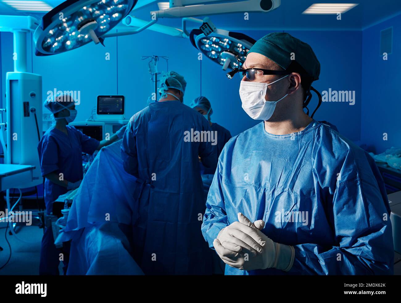 Chirurgia. Chirurgo professionista in scrub blu e maschera protettiva in piedi in sala operatoria durante l'intervento chirurgico con infermieri e assistenti Foto Stock