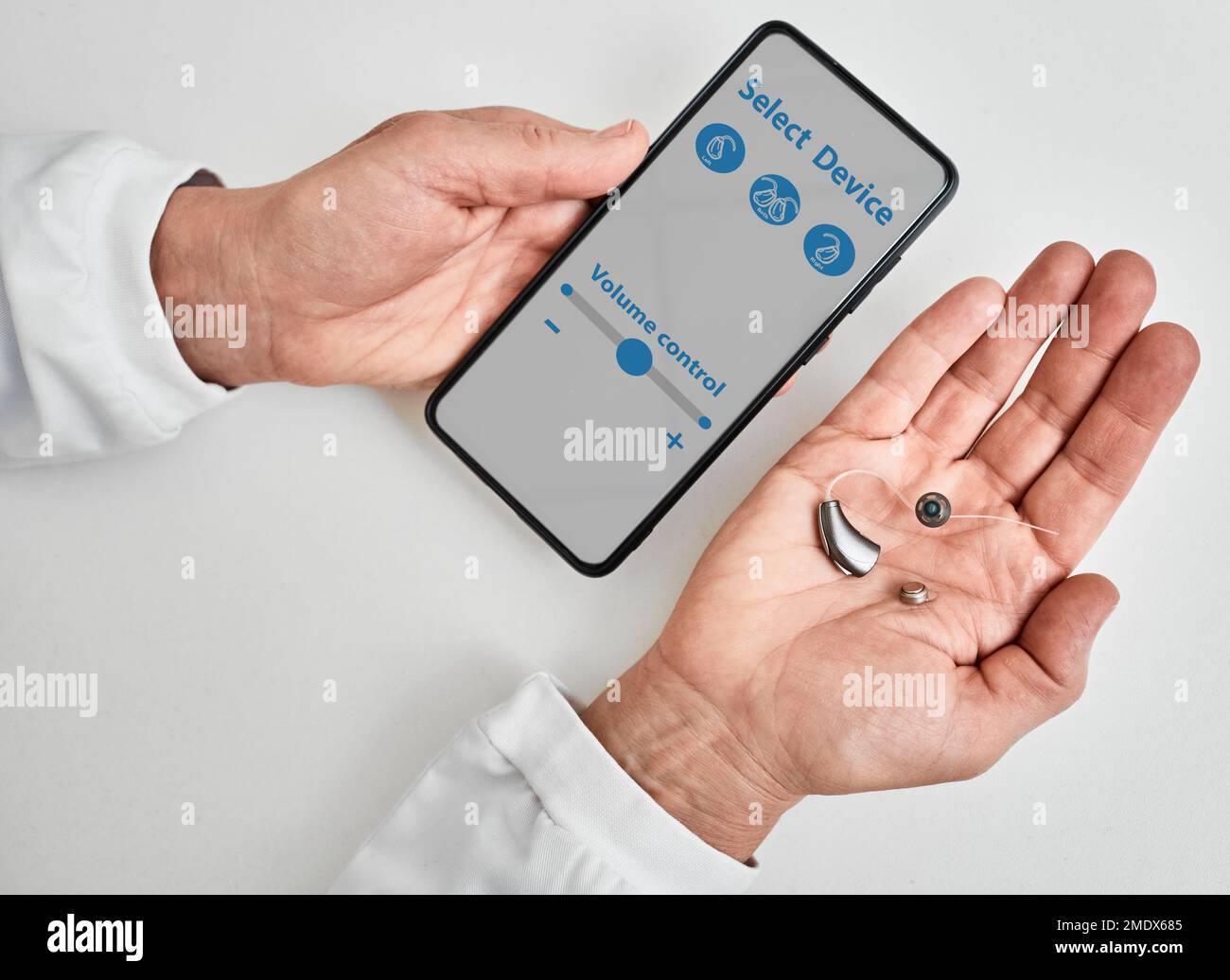 Medico audiologo che mostra l'app per smartphone per regolare l'apparecchio acustico tenendo lo smartphone in una mano e l'apparecchio acustico BTE in un'altra. Gestire gli apparecchi acustici Foto Stock