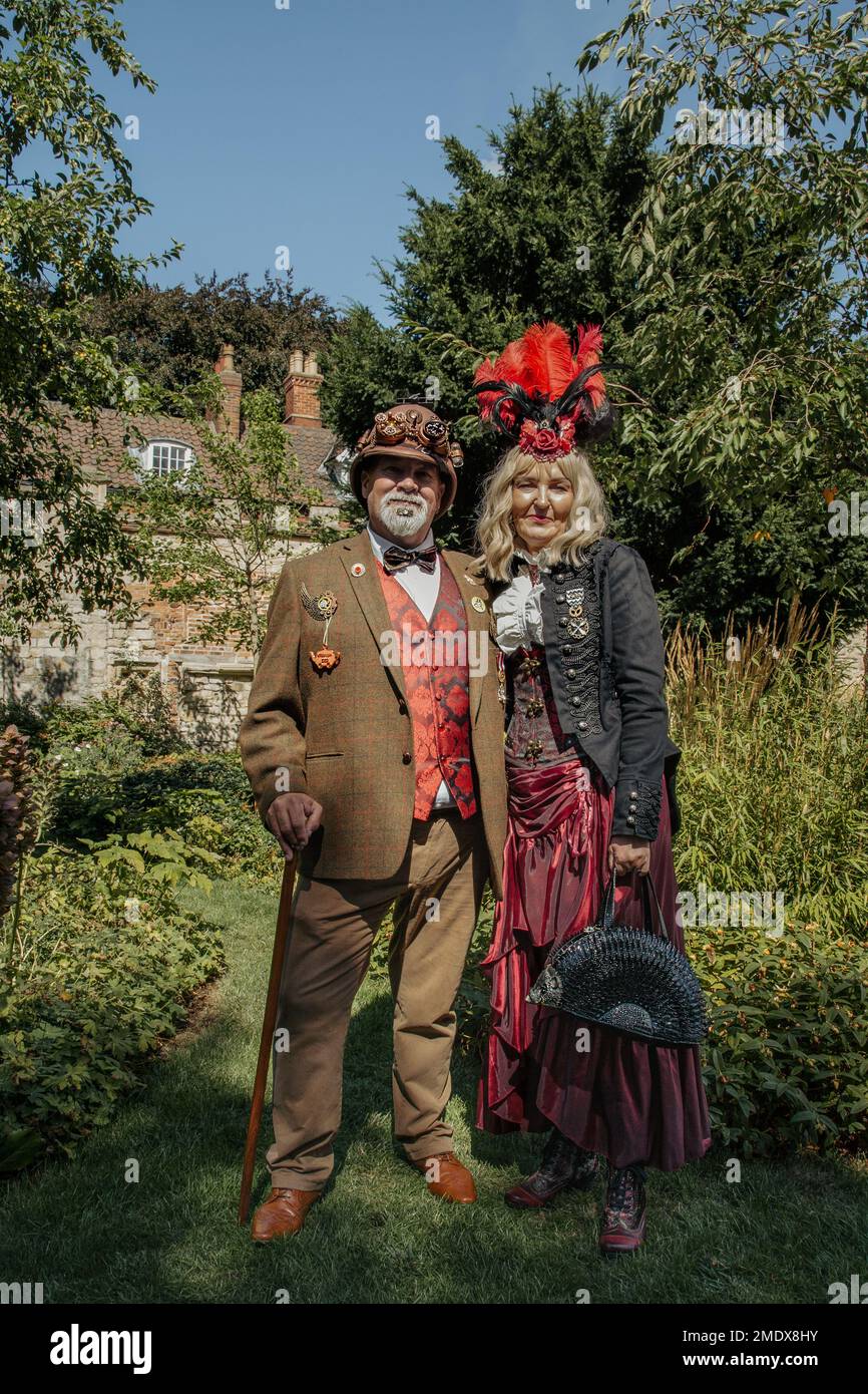 Una coppia eccentrica di mezza età in piedi nel giardino di una casa di campagna. Coppia di steampunk di mezza età ben vestita. Vittoria della lotteria, concetto di viaggio. Foto Stock