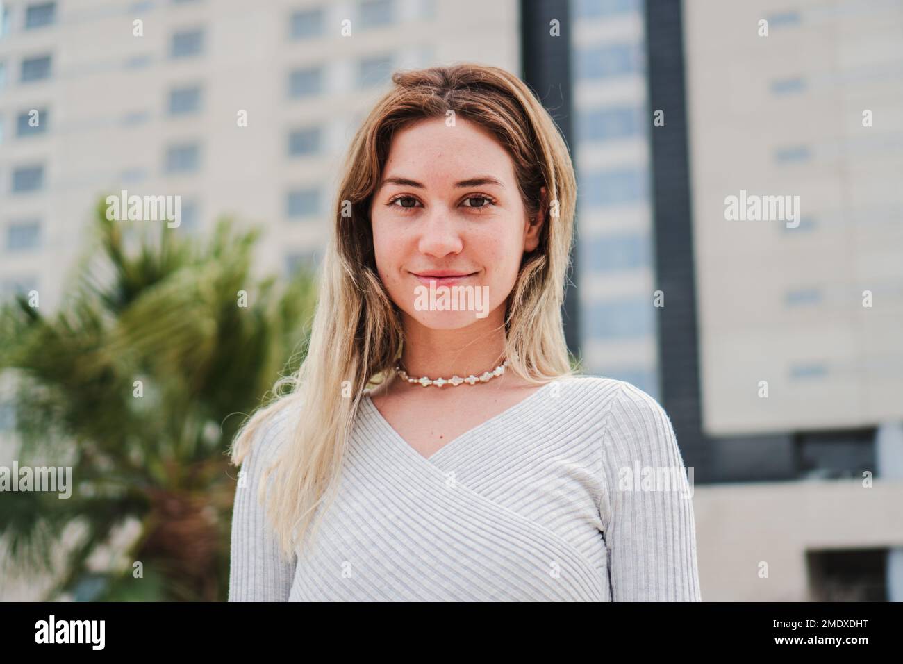 Primo piano ritratto di una felice bionda donna sorridente guardando la macchina fotografica e toccando i suoi capelli. Vista frontale di giovane donna isolata con denti perfetti che ridono all'aperto. Foto di alta qualità Foto Stock