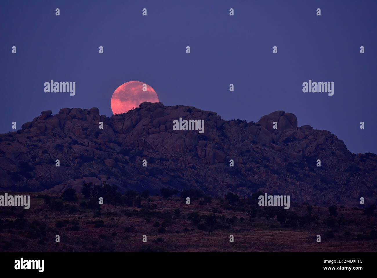 Luna piena dietro colline rocciose all'alba, Wichita Mountains Wildlife Refuge, Oklahoma Foto Stock
