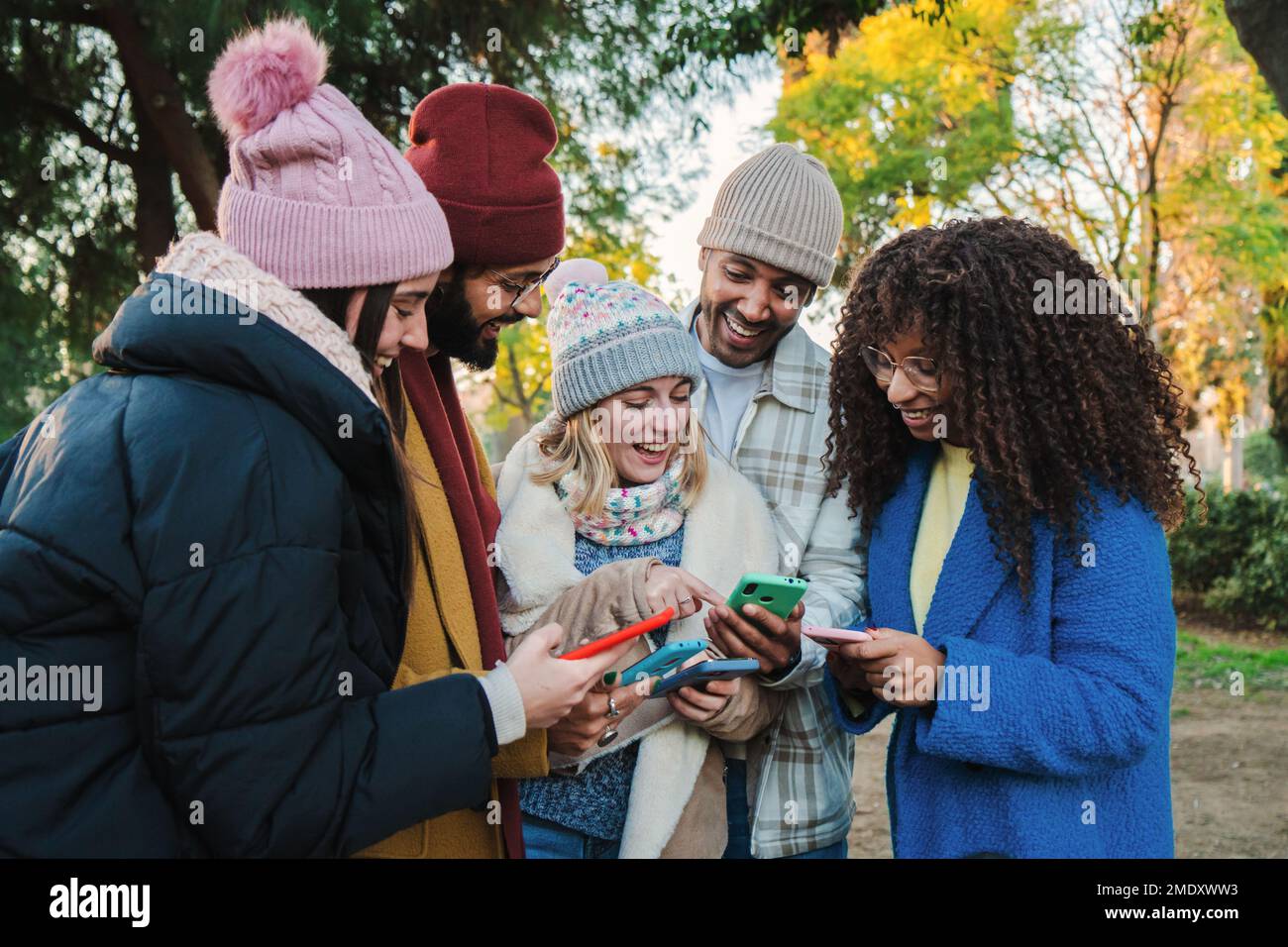 Ritratto di un gruppo di giovani fidanzati multirazziali che guardano video su un'app di social media utilizzando un cellulare con abiti autunnali. Persone multietniche che si divertono con i loro smartphone. Concetto di comunicazione. Foto di alta qualità Foto Stock