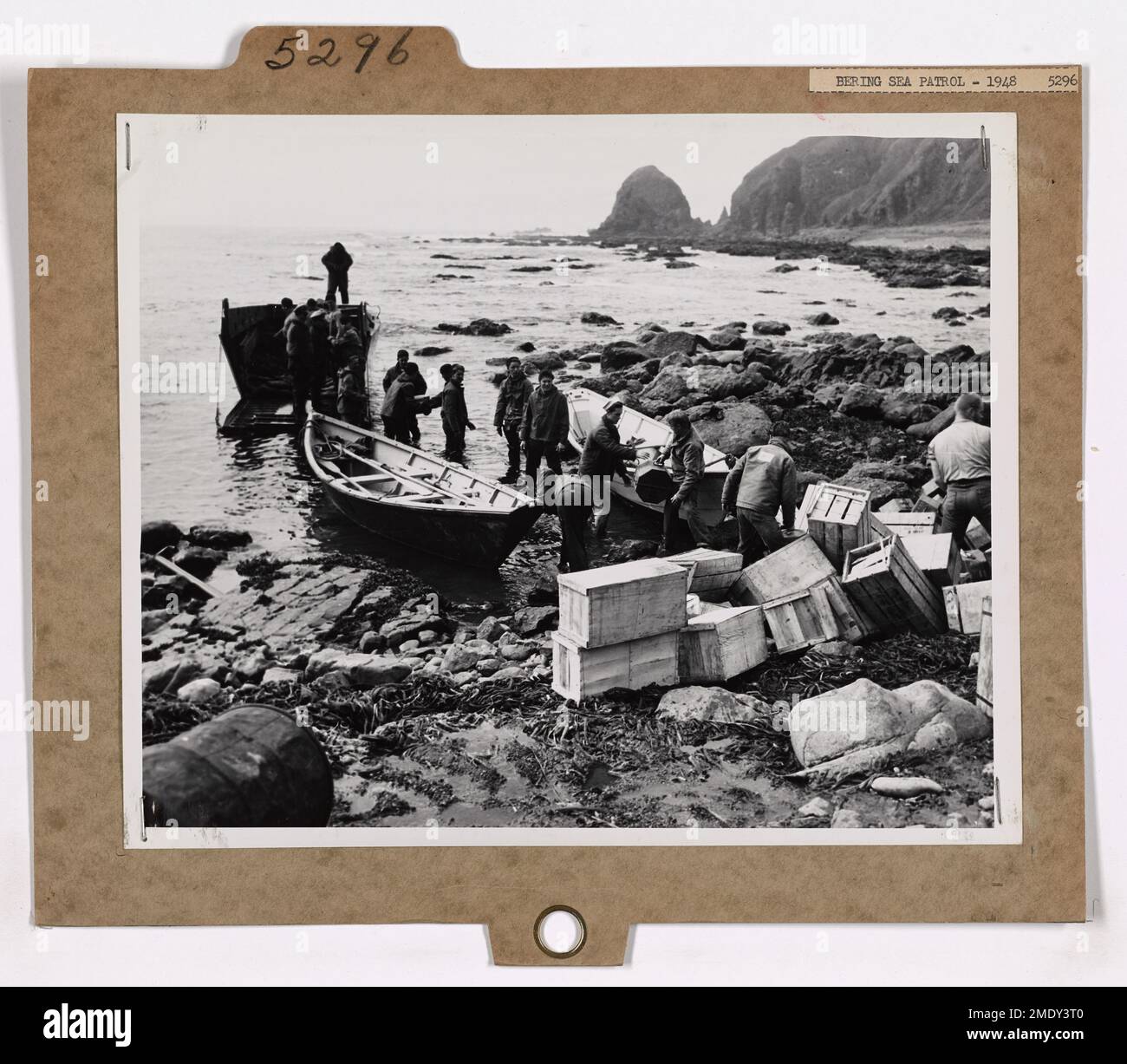 Questa immagine mostra la Cutter NORTHWIND che scarica rifornimenti, cibo, carburanti e posta per la stazione Loran della Guardia Costiera ad Attu. A causa del terreno impegnativo, i rifornimenti vengono scaricati da nave a chiatta in mari accidentati e poi trasferiti sulla spiaggia di roccia vulcanica. L'arrivo del NORTHWIND in questo luogo isolato è stato accolto con una celebrazione. Foto Stock
