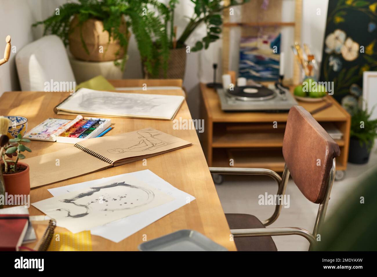 Carte e blocco note con schizzi disegnati dall'artista in casa studio con tavolo, sedia, piante verdi, acquerelli, lettore di dischi e altro Foto Stock