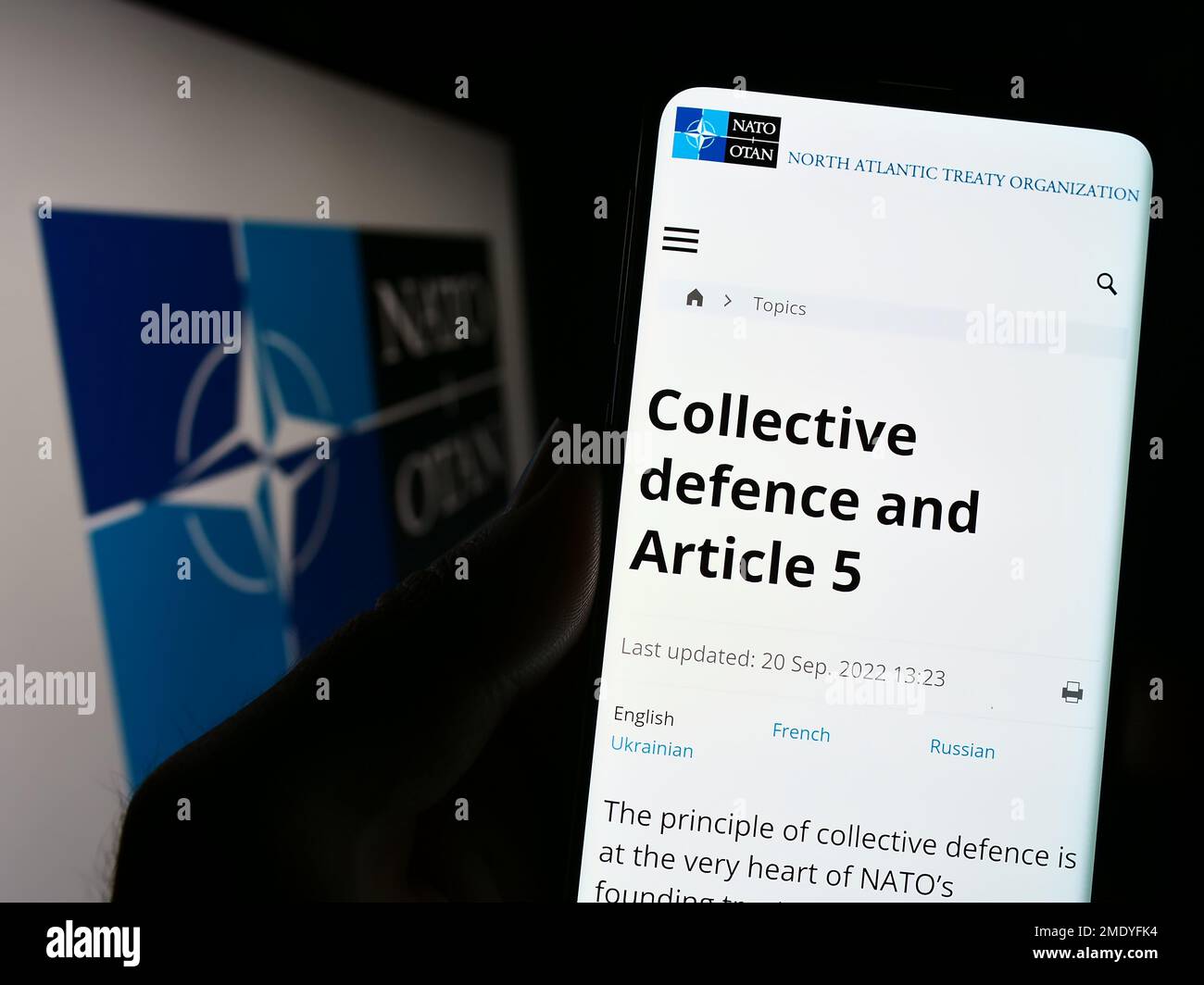 Persona che tiene il cellulare con la pagina web della NATO (North Atlantic Treaty Organization) sullo schermo di fronte al logo. Messa a fuoco al centro del display del telefono. Foto Stock