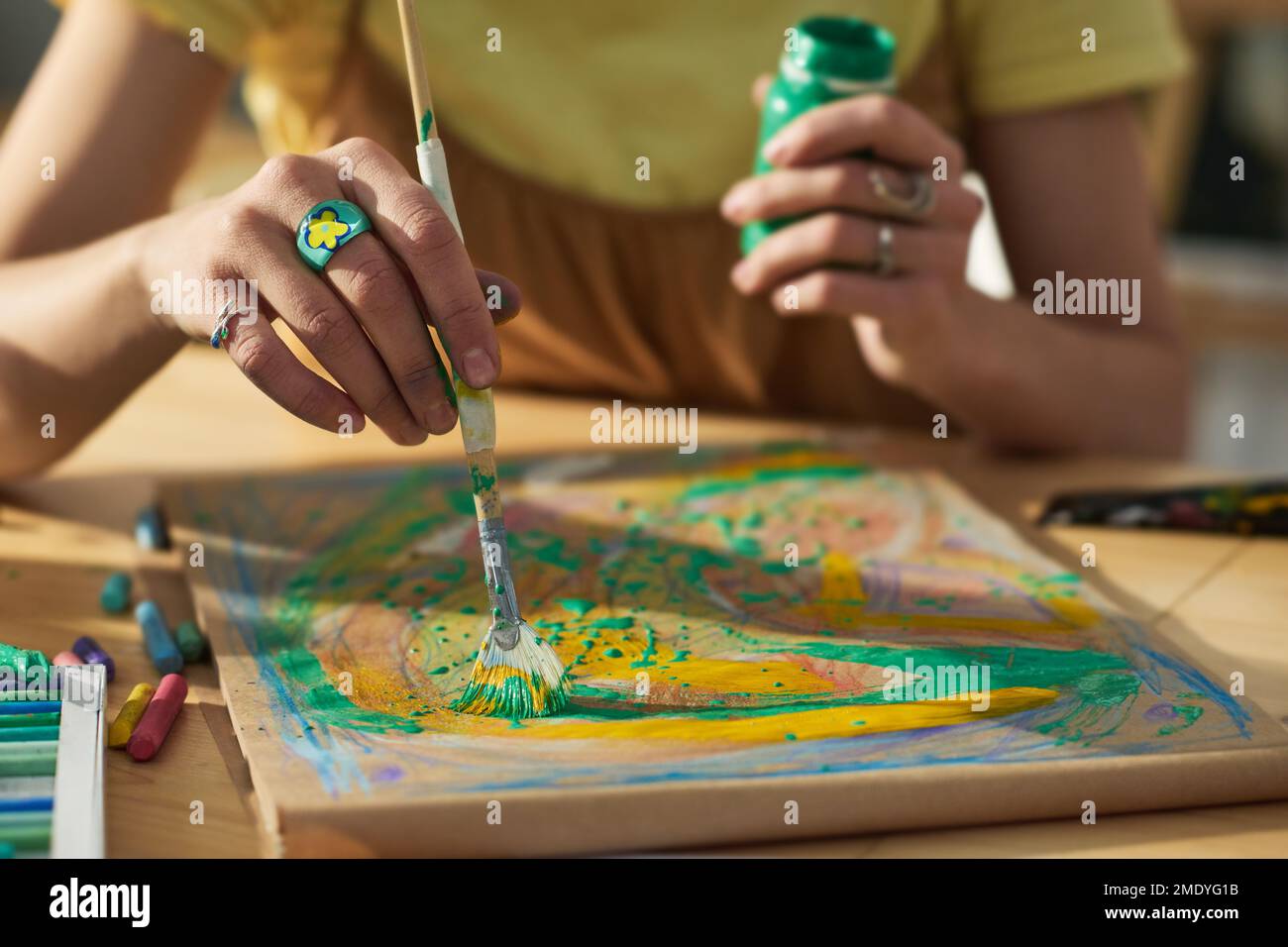 Primo piano delle mani di una giovane donna creativa con pennello e gouache creando nuove opere d'arte su carta mentre si è seduti sul posto di lavoro in studio Foto Stock