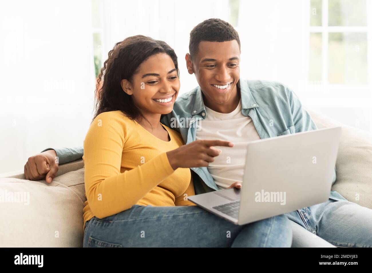 Sorridente giovane afro-americano uomo e donna puntano il dito contro il portatile, hanno videochiamata, chat online Foto Stock