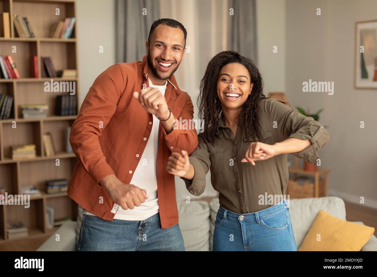 Gioiosi sposi afroamericani che si divertono e ballano insieme, celebrando il movimento o l'anniversario nel salotto interno Foto Stock