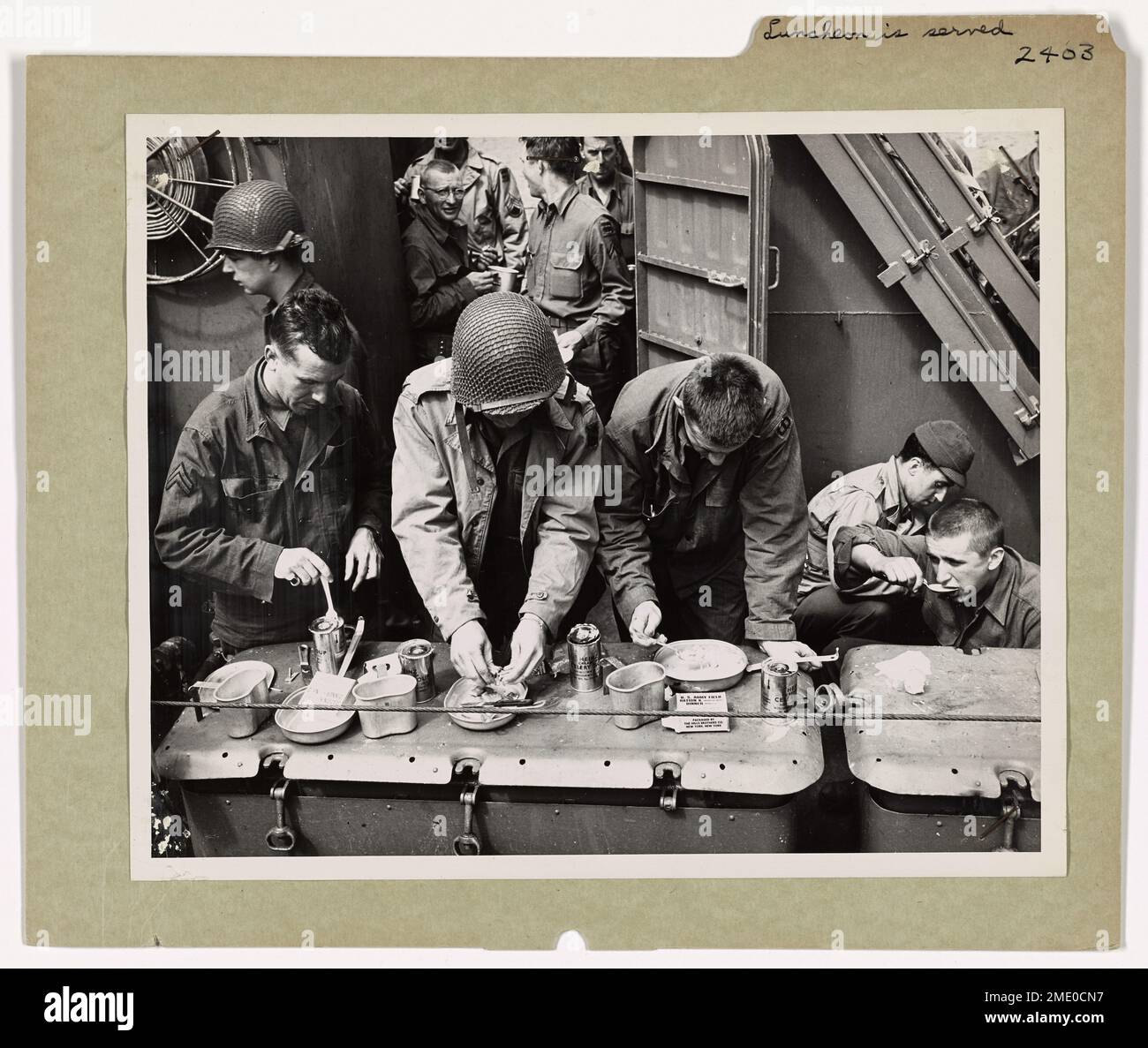 Fotografia dei soldati americani che catturano le loro razioni K e la zuppa di sedano dalla cima di una scatola pronta da 20 mm. Il pranzo viene servito nella Manica. Vieni a prendere i ragazzi, mentre il gettin è buono. Attraversando il canale inglese a bordo di una Guardia Costiera 'Elsie' (o LCI), i soldati americani catturano le loro razioni K e la zuppa di sedano dalla cima di una scatola pronta da 20 mm. Avanti si trova la Costa della Francia, ma per il momento il chow è la cosa importante. Non si può combattere uno stomaco vuoto. Foto Stock